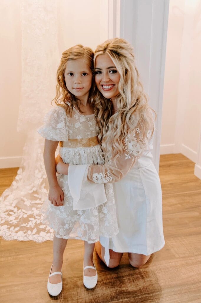 A bride bends down to pose for a photo with her flower girl.